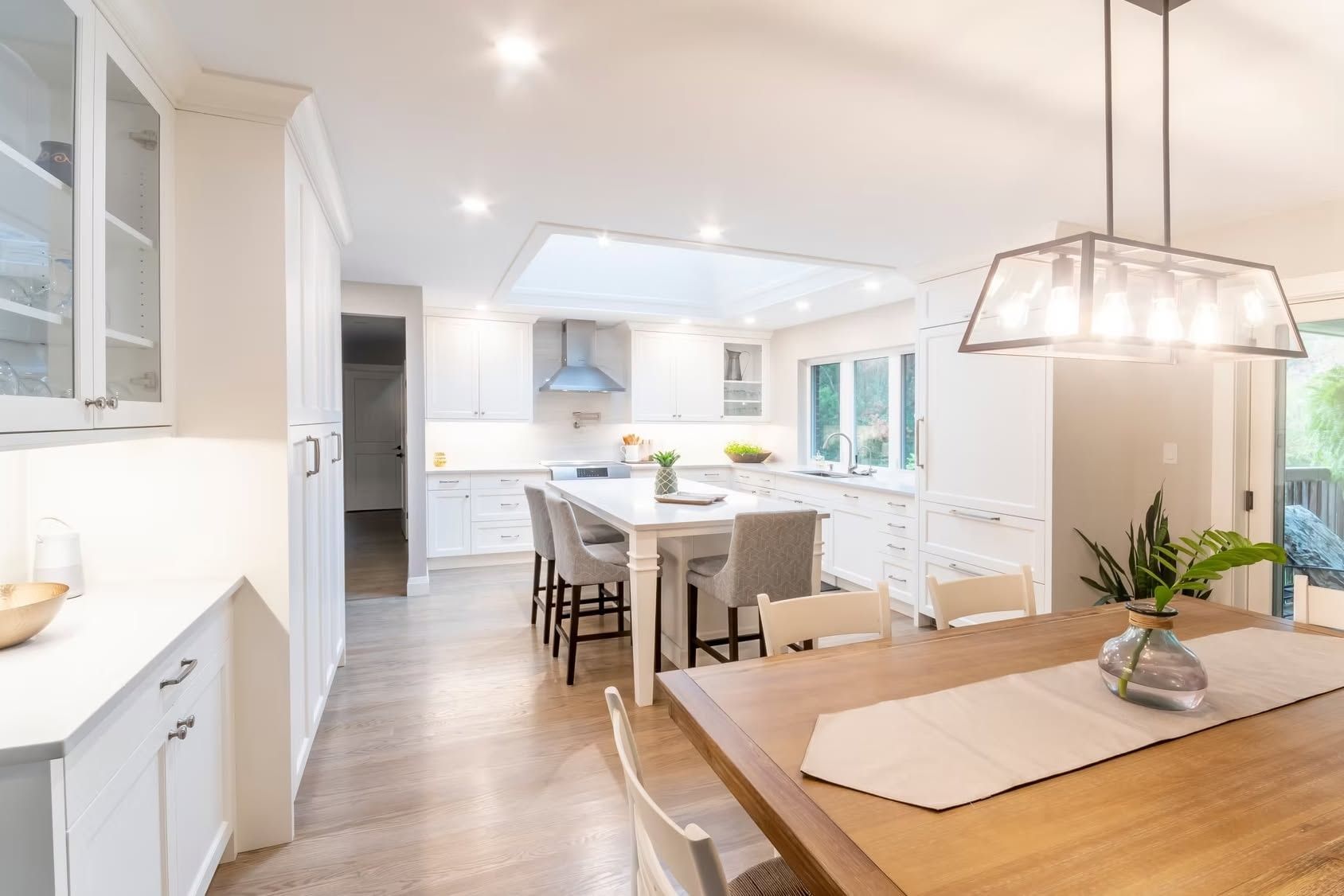 White kitchen with an island, stools and a wood dining table.